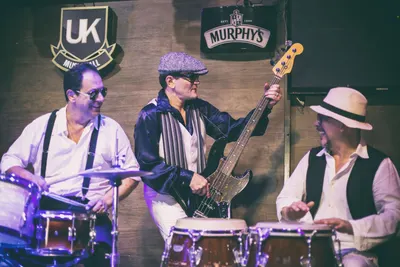 Baterista, baixista de boina e percussionista de chapéu
