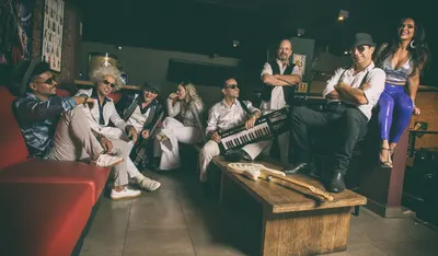 A banda no sofá vermelho, três vocalistas à frente do microfone