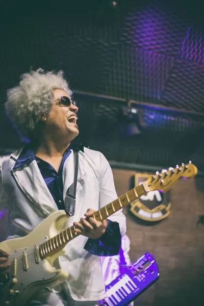 Guitarrista de peruca afro grisalha cantando, foto vertical
