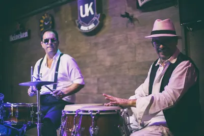 Dois percussionistas lado a lado, bateria e congas