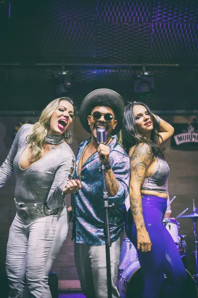 Close vertical do trio de vocalistas cantando ao microfone